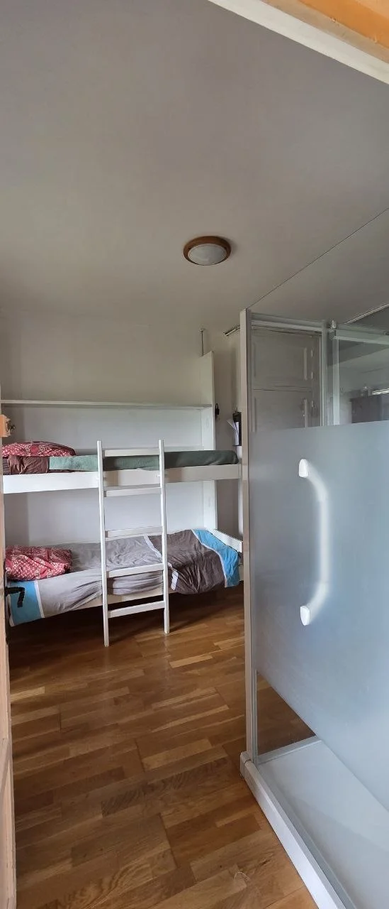 Une chambre de La Maison du Peintre : lits superposés en bois clair, parure sobre grise et bleue, parquet, lumière douce.