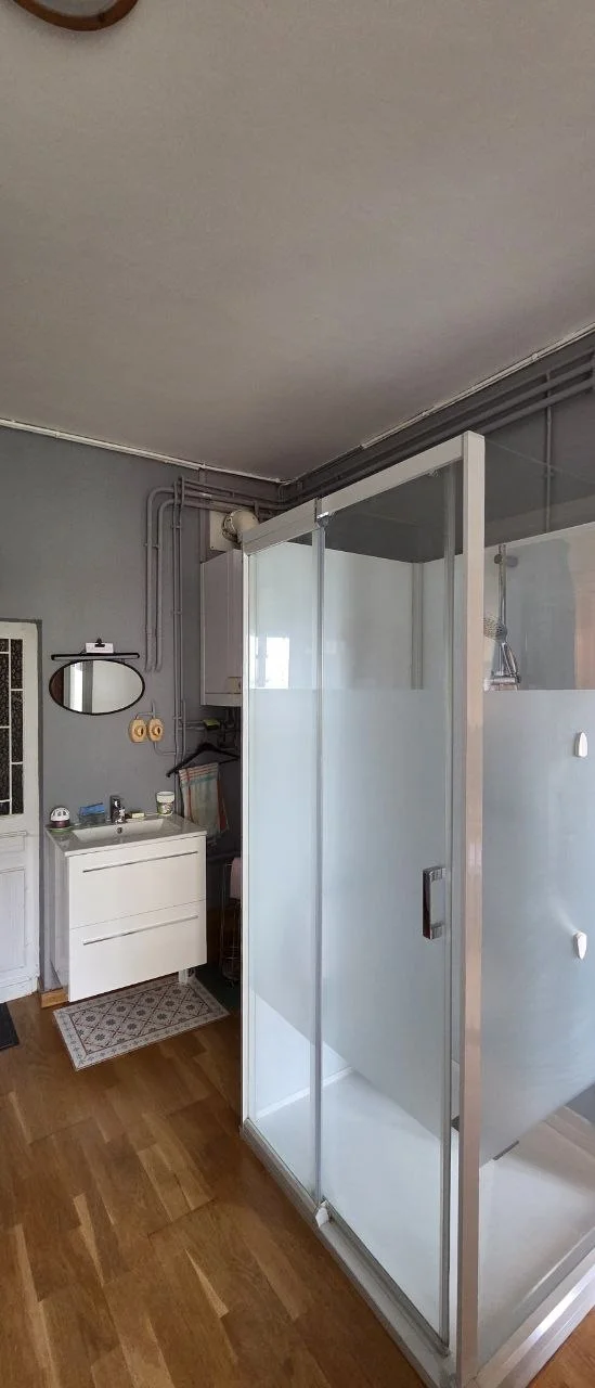 Salle d'eau moderne, douche italienne vitrée, vasque blanche et miroir ovale.